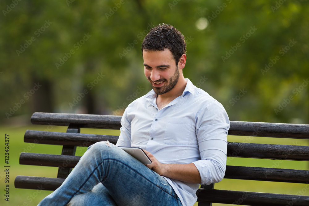 Young businessman is sitting at the park and using digital tablet.
Young businessman is sitting at the park and using digital tablet.