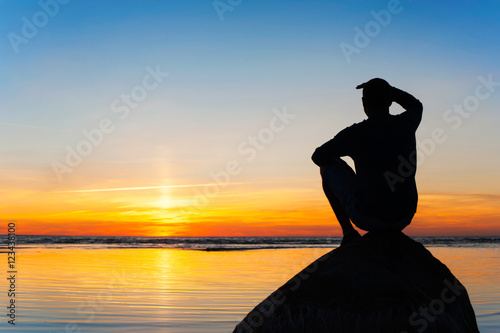 Young man silhouette sitting on the rock at sunset background