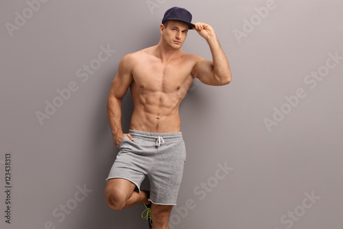Shirtless young guy leaning against a gray wall