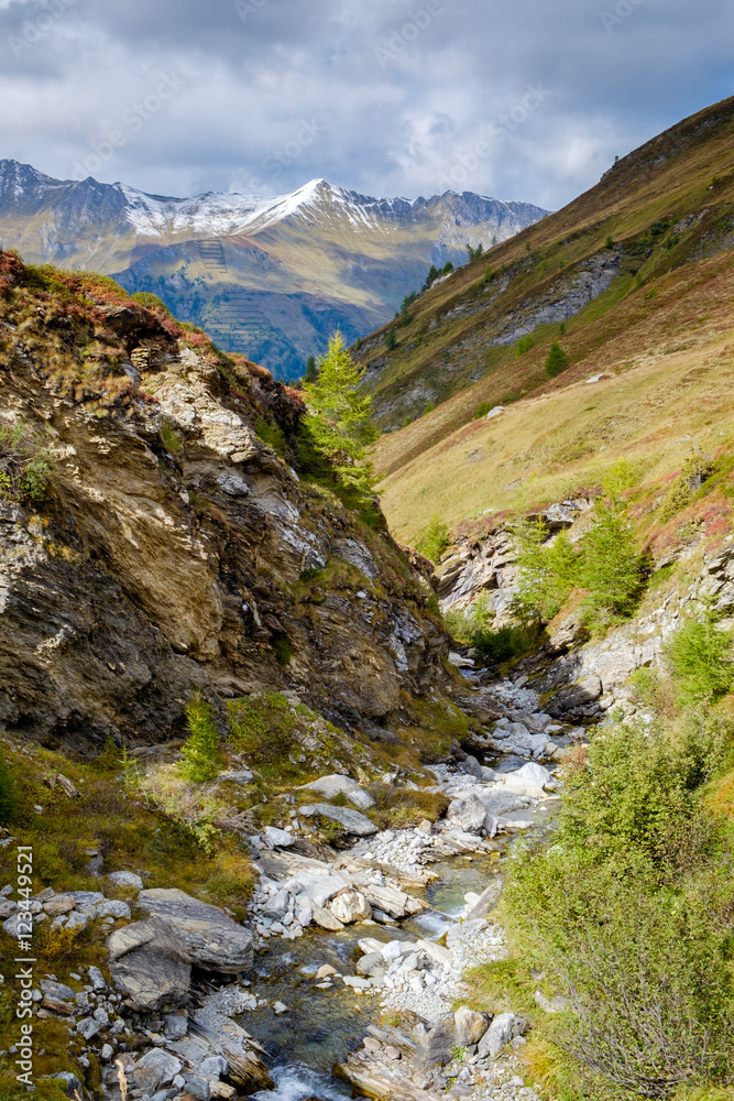 picturesque valley, smal winding stream and snowed moutain peaks in the Austrian Alps in autumn