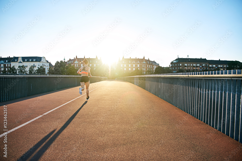Woman running down bridge with long shadow in back
