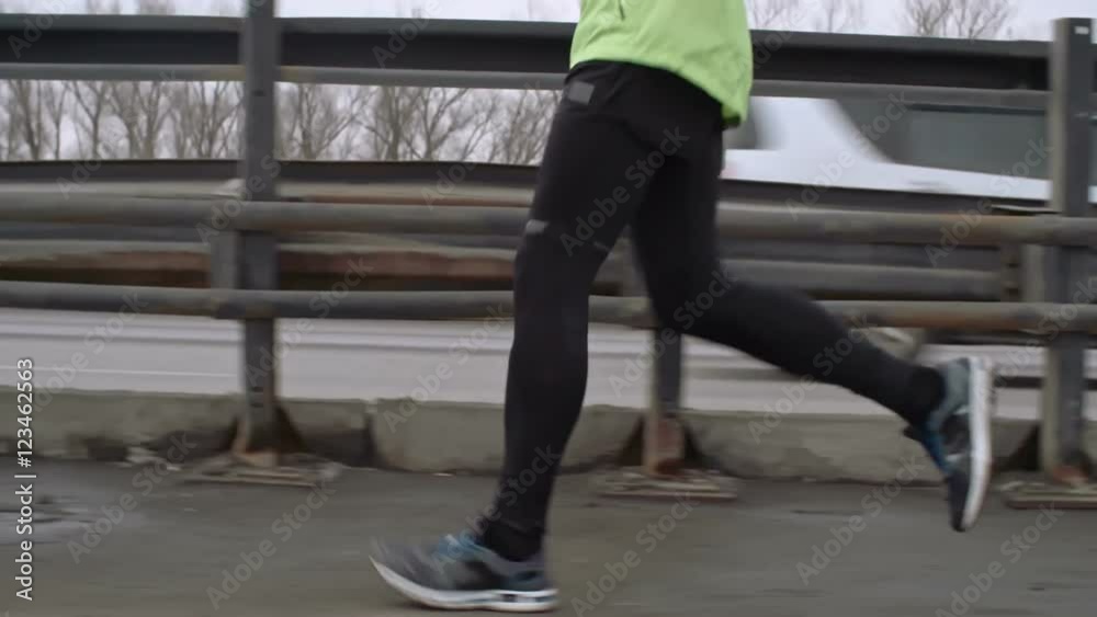MS Tracking shot tilt up of young bearded athlete running across bridge during marathon training, cars passing by MS Tracking shot tilt up of young bearded athlete running across bridge during marathon training, cars passing by