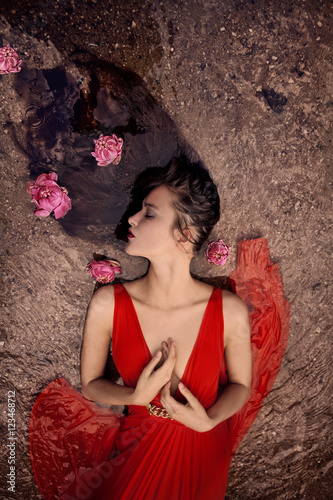 Woman wearing red dress lying on ground with pink flowers 