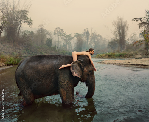 Naked woman lying on elephant wading in water  photo
