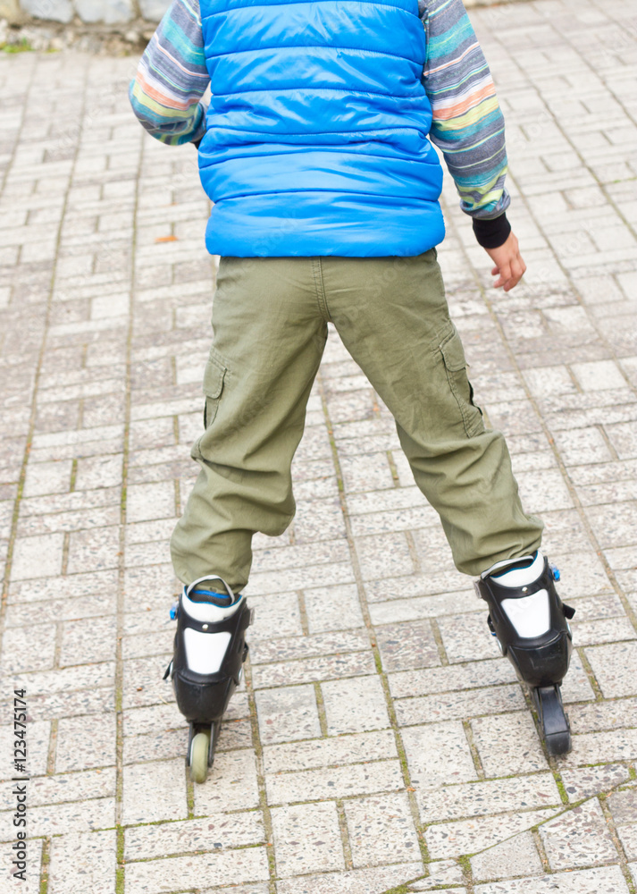 A young cute boy in a blue shirt with roller blades learning to skate on the road. Kids and sport. Hobby.