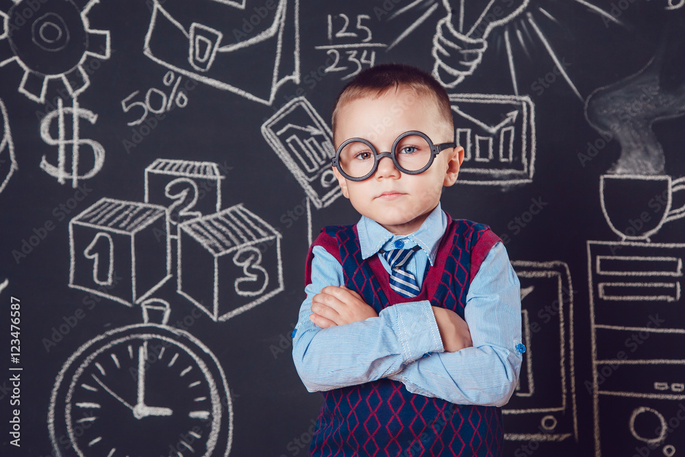 Little boy as businessman or teacher with glasses standing her hands folded on a dark background pattern Little boy as businessman or teacher with glasses standing her hands folded on a dark background pattern