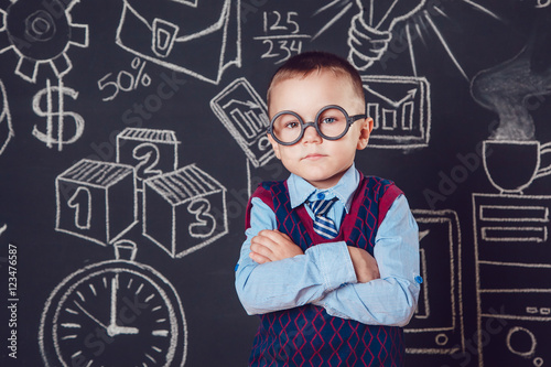 Little boy as businessman or teacher with glasses standing  her hands folded on a dark background  pattern