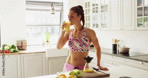 Fit healthy young woman with a toned shapely body standing drinking a glass of freshly prepared fruit juice in a high key kitchen in a health and fitness concept