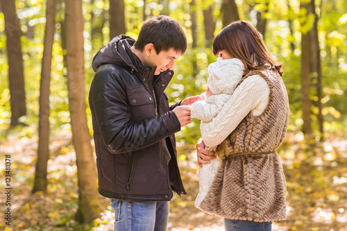 young family with their newborn baby spending time outdoor in the autumn park.