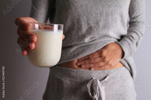 Woman with stomach pain holding a glass of milk. Dairy Intolerant person. Lactose intolerance, health care concept. photo