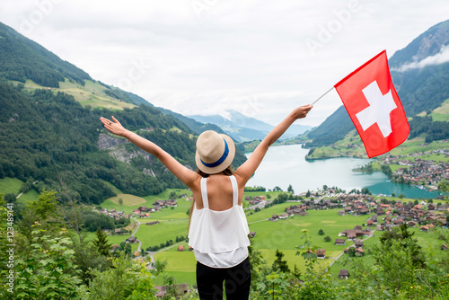 Young woman with swiss flag enjoying great landscape view on the valley with lake and village in Switzerland. photo