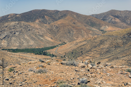 Summer daylight scene of a valley near Tindaya, showing mountains, clear blue sky and surprising for Fuerteventura some green vegetation.