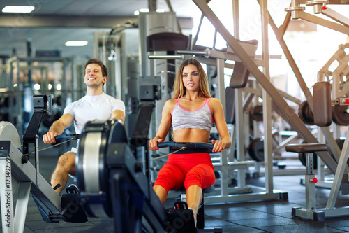 Athletic man and woman training on row machine in gym