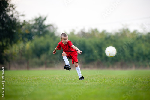 Little football player in red uniform shooting the ball © marritch