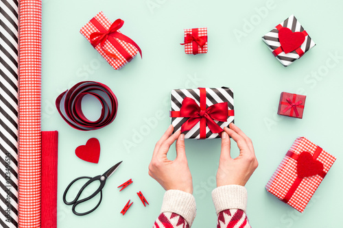Female hands tying a red bow. Gifts' wrapping ideas. Present boxes on a mint background. Top view.
