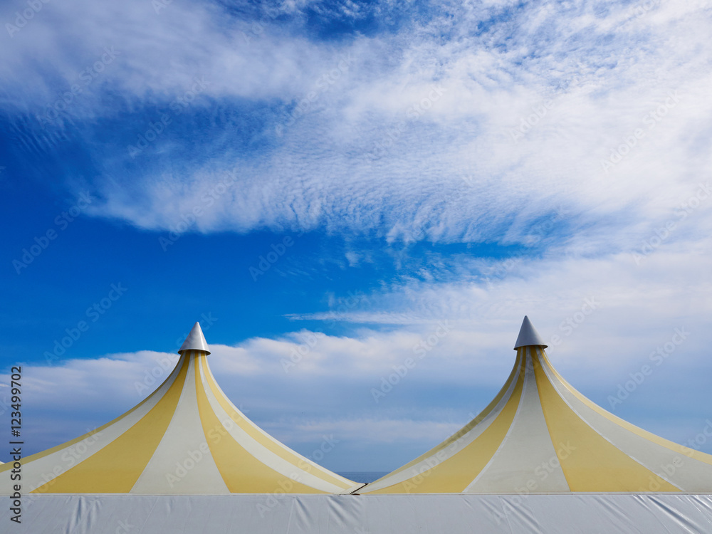 Upper part of a big colorful plastic tent. Blue sky and white clouds in background.