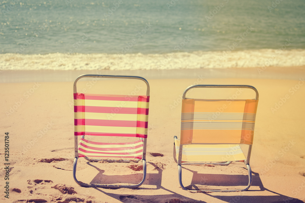 Back view of two beach chairs on sandy beach sunny outdoors background. Back view of two beach chairs on sandy beach sunny outdoors background.