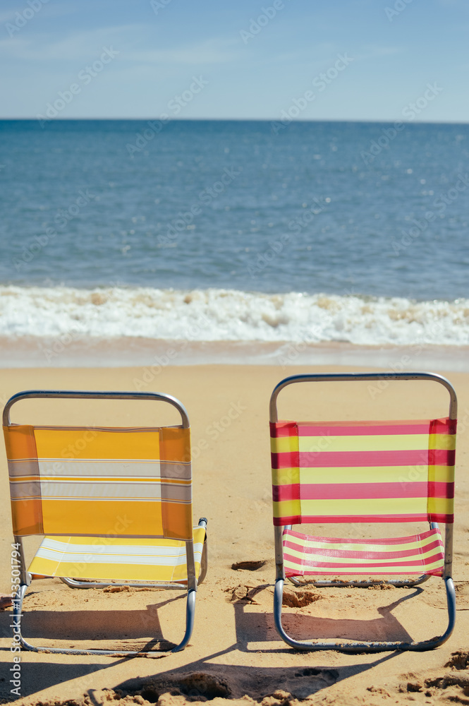 Back view of two beach chairs on sandy beach sunny outdoors background. Back view of two beach chairs on sandy beach sunny outdoors background.