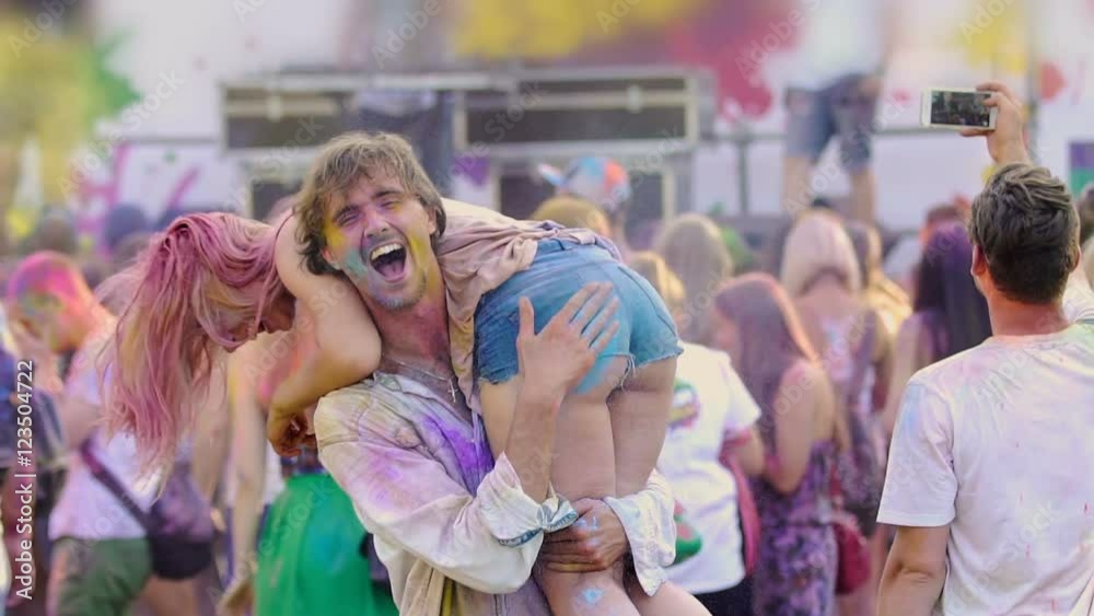 Young drunk man holding sexy woman on shoulders, dancing at Holi fest, crazy fun Young drunk man holding sexy woman on shoulders, dancing at Holi fest, crazy fun