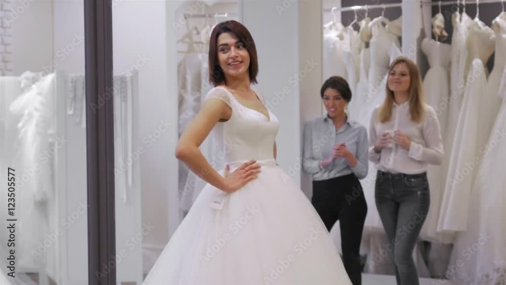 pretty young woman is choosing a wedding dress in the shop and the shop assistant is helping her. Group of Girls in wedding shop. pretty young woman is choosing a wedding dress in the shop and the shop assistant is helping her. Group of Girls in wedding shop.