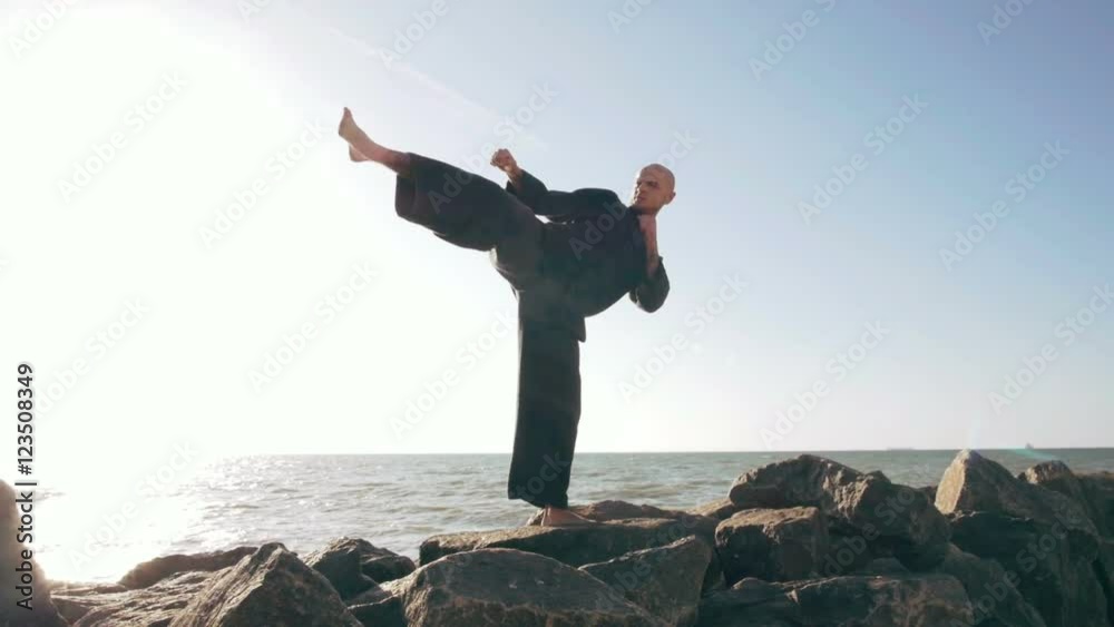 Two male karate fighters posing on stones sea background, slow motion