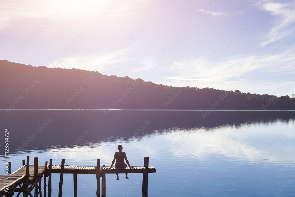 Happy woman sitting on a pier getting inspired by nature