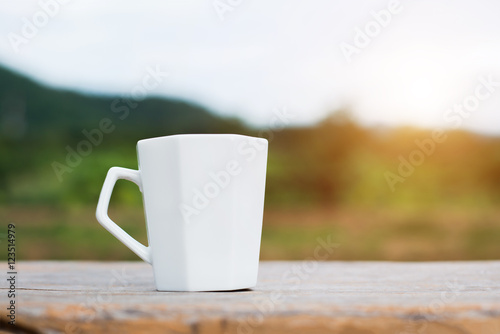 White cup of hot coffee on mountain natural green background.