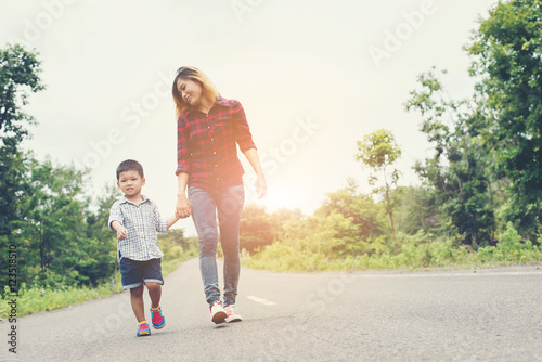 Happy mom holding hand with his son walking on the street.