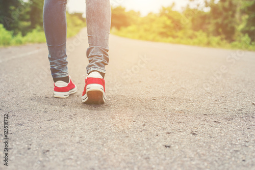 Woman feet with red sneaker shoes walking on the roadside.