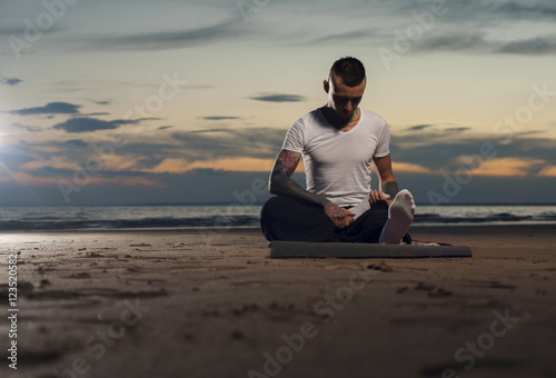 Serene young man practicing yoga on the beach