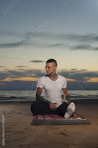 Calm young man doing yoga on the beach at sunset