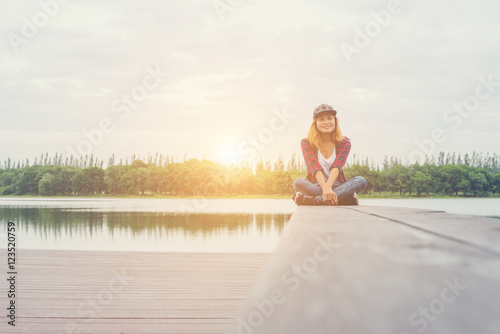 Young hipster woman sitting on pier and smiling at the camera.