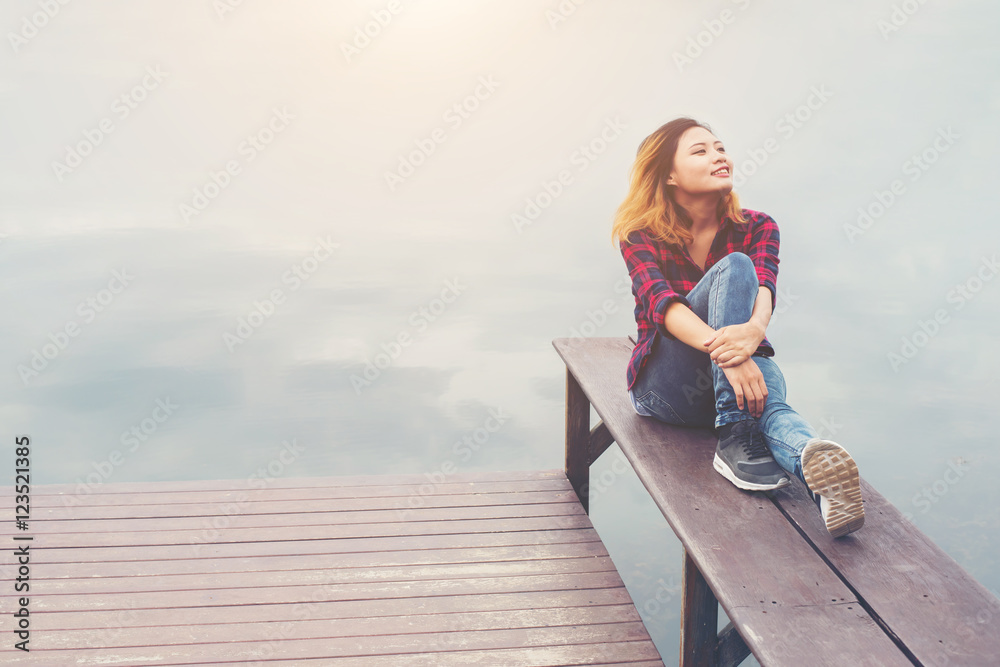 Happy young hipster woman sitting at the pier lake,relaxing enjo