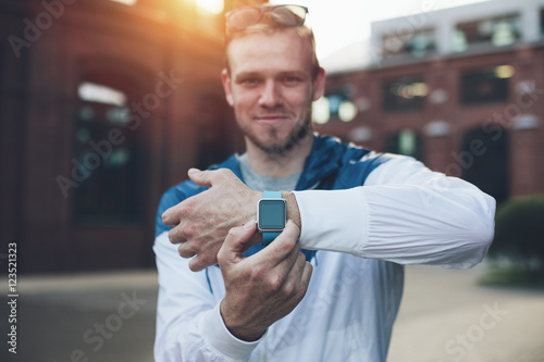 Cheerful man showing his smart watches on the wrist at sunset photo