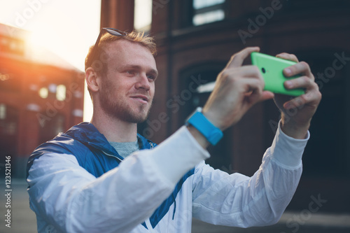 Young cheerful man taking photo with smartphone on the street photo