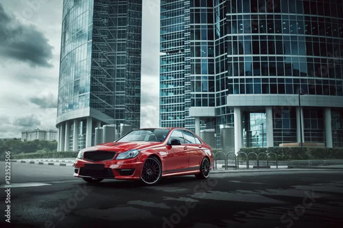 Obraz Czerwony samochód zostaje na asfaltowej drodze w mieście przy dniem