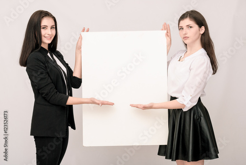 Two happy smiling young business women carrying big blank signbo