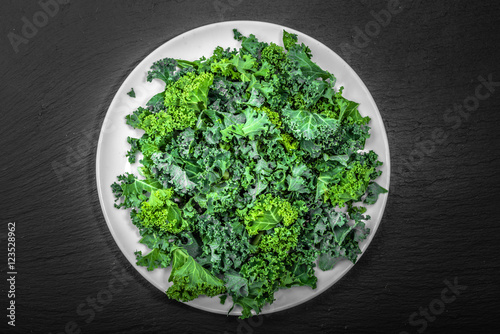 Green kale vegetable leaves on plate on black background