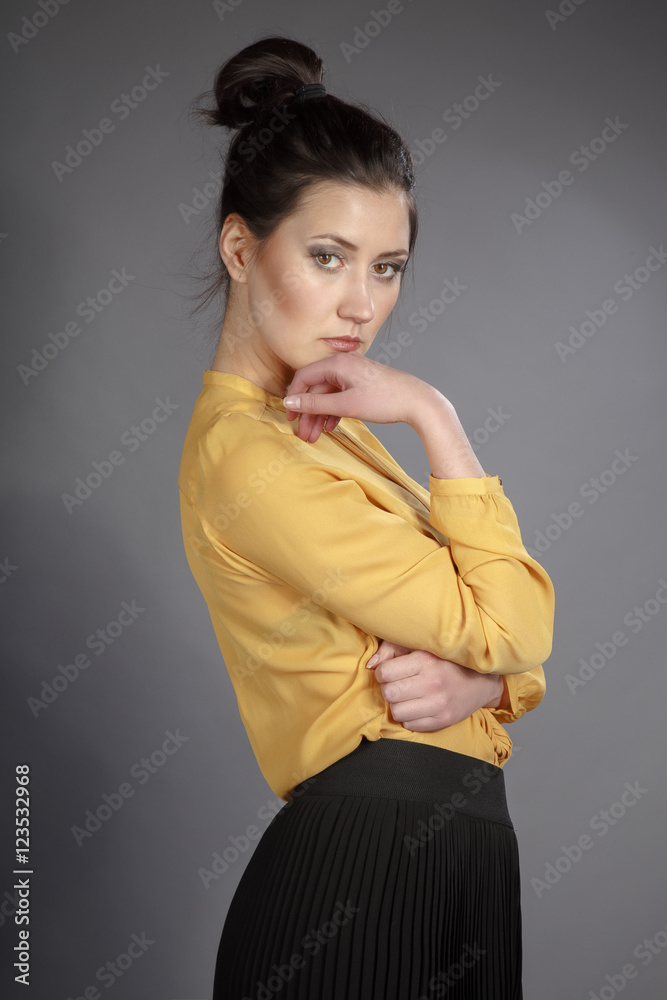 Fototapeta premium Portrait of beautiful girl in Studio in a yellow blouse and black skirt on a gray background