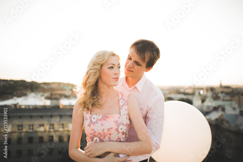 Close up portrait of happy smiling couple in love posing on roof with big balls. Landscape city