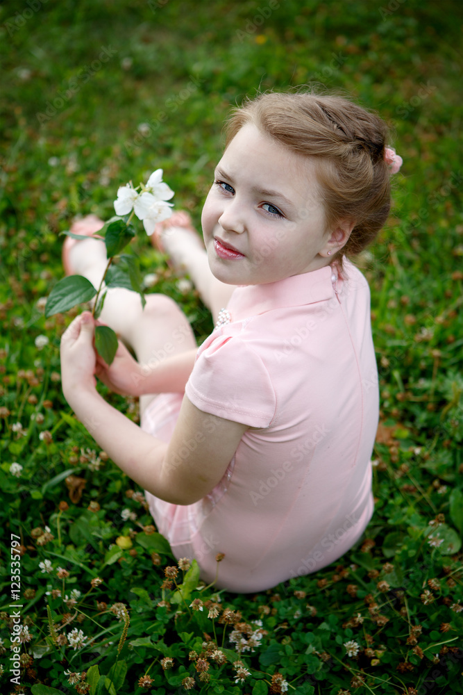 Portrait of a beautiful girl outdoors sitting on grass with flowers