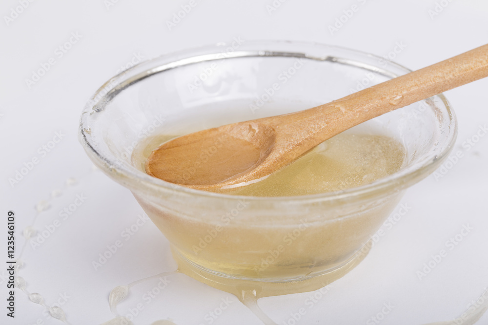 Bee honey in a glass bowl and wooden spoon on white background Bee honey in a glass bowl and wooden spoon on white background
