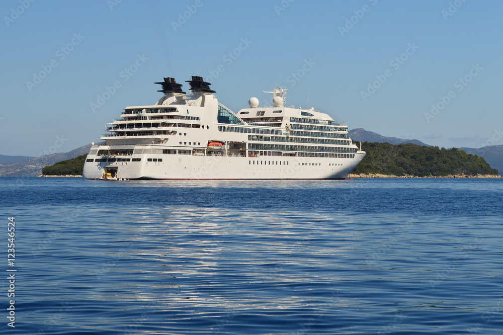 Big white cruise ship in calm blue sea, green islands and blue sky on the background