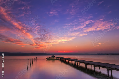 Stunning water reflection sunset with wooden pier and boat