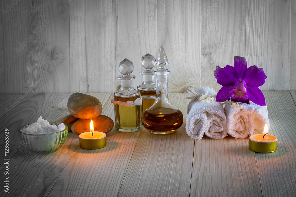 Bottles of aromatic oils with candles, pink orchid, stones and white towel on vintage wooden background with vignette,spa treatment concept Bottles of aromatic oils with candles, pink orchid, stones and white towel on vintage wooden background with vignette,spa treatment concept