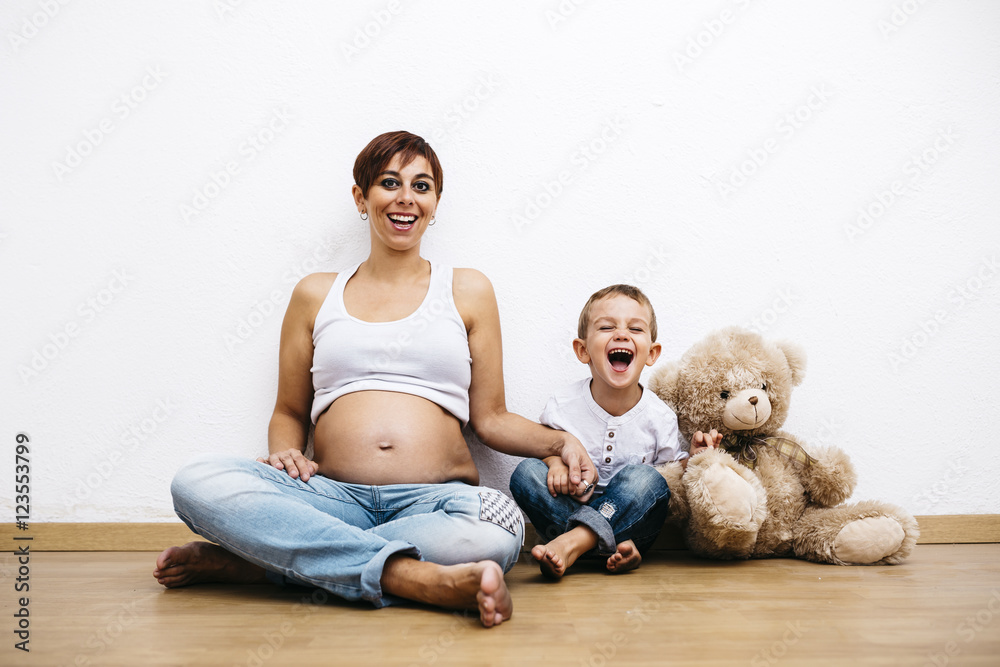 Pregnant mother and little son sitting on floor, laughing