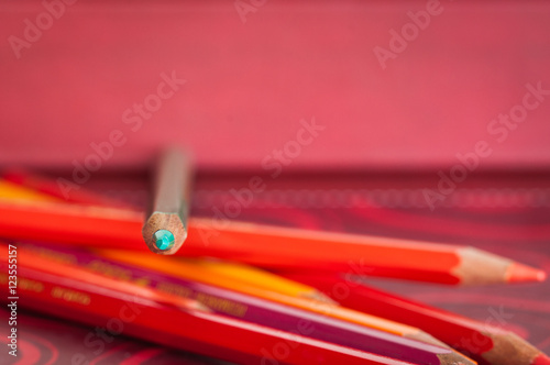 matita colore verde acquamarina sopra altri pastelli rossi e arancioni.  Sfondo rosso; immagine a fuoco sulla punta della matita Stock Photo