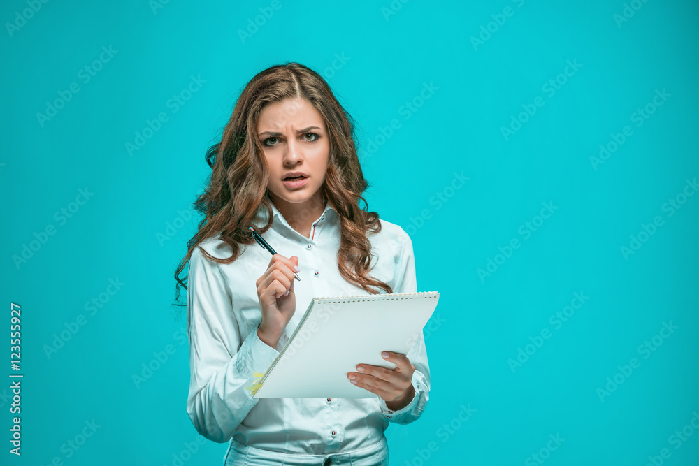 Fototapeta premium The thoughtful young business woman with pen and tablet for notes on blue background