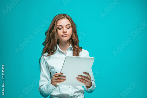 The thoughtful young business woman with pen and tablet for notes on blue background