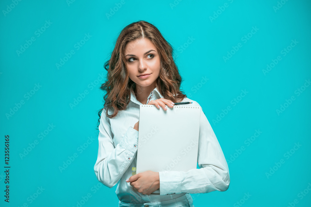 Fototapeta premium The smiling young business woman with pen and tablet for notes on blue background